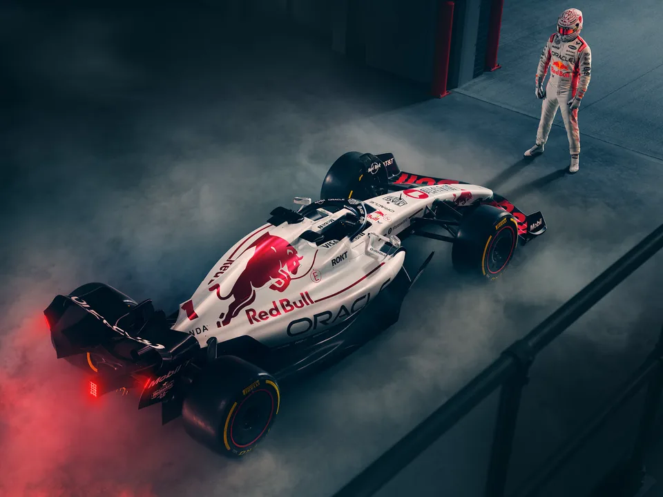 The white RB21 from above in a dark garage, Verstappen standing beside it in red haze.